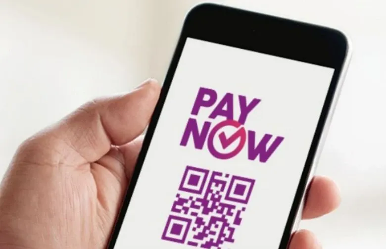 A hand holding a mobile phone with the words PayNow and a QR code on it's screen